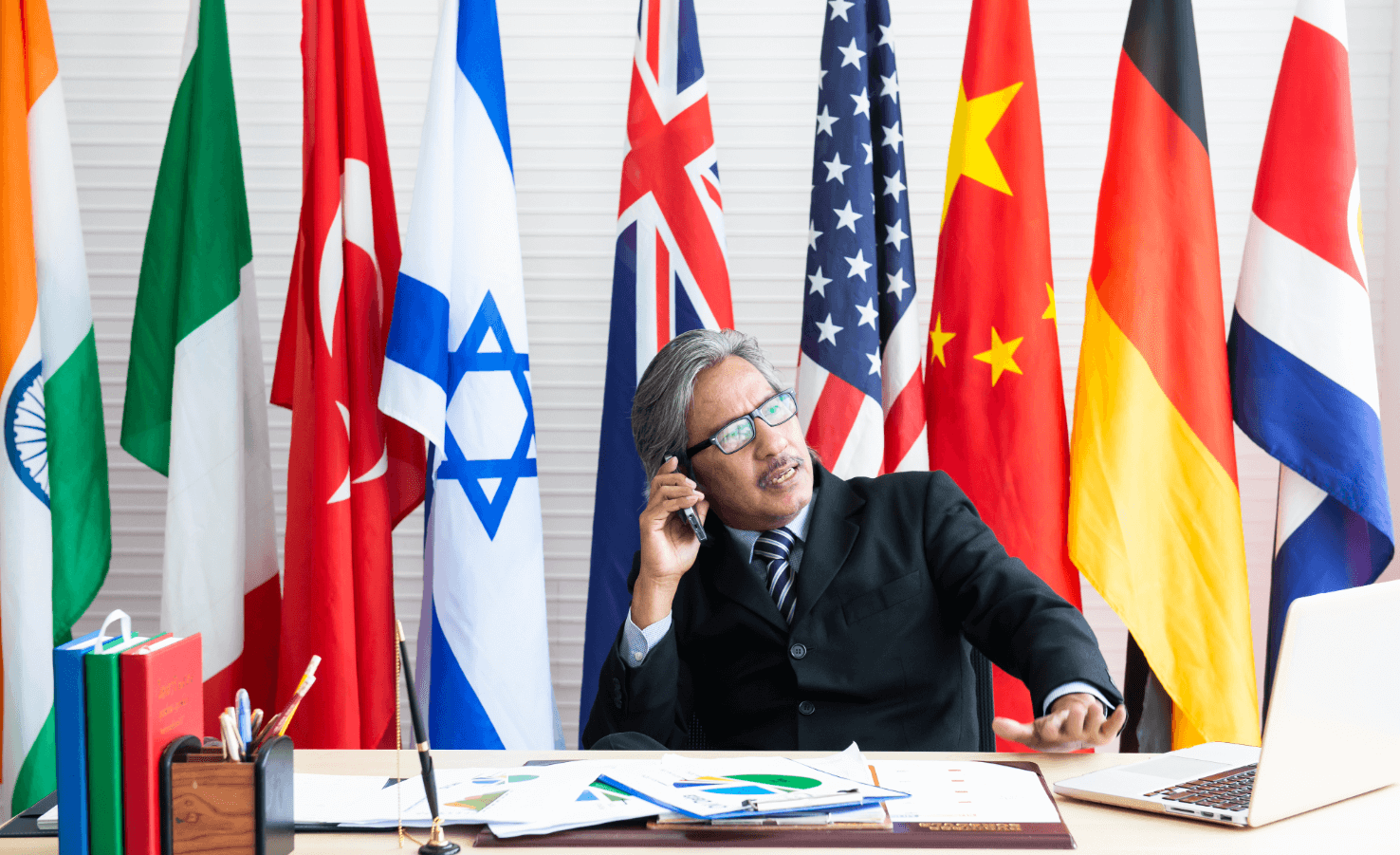 Government official on phone with laptop, seated before international flags, symbolising global political Instagram influence